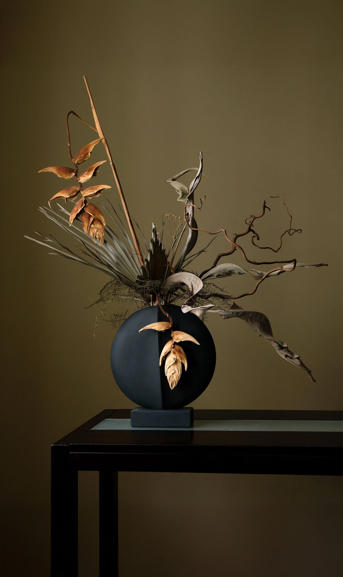 Decorative arrangement of dried plants in a black Guggenheim vase
