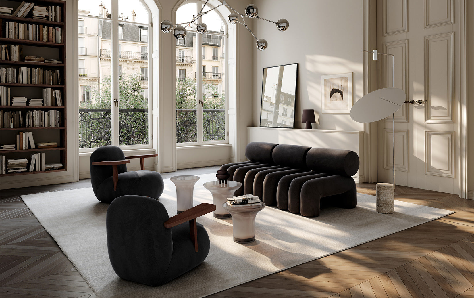 A modern living room featuring a dark charcoal gray modular Foku sofa, two Toe armchairs, a low Trumpet coffee table in glass. The room is styled with classic cream walls, tall bookshelves, and large arched windows.