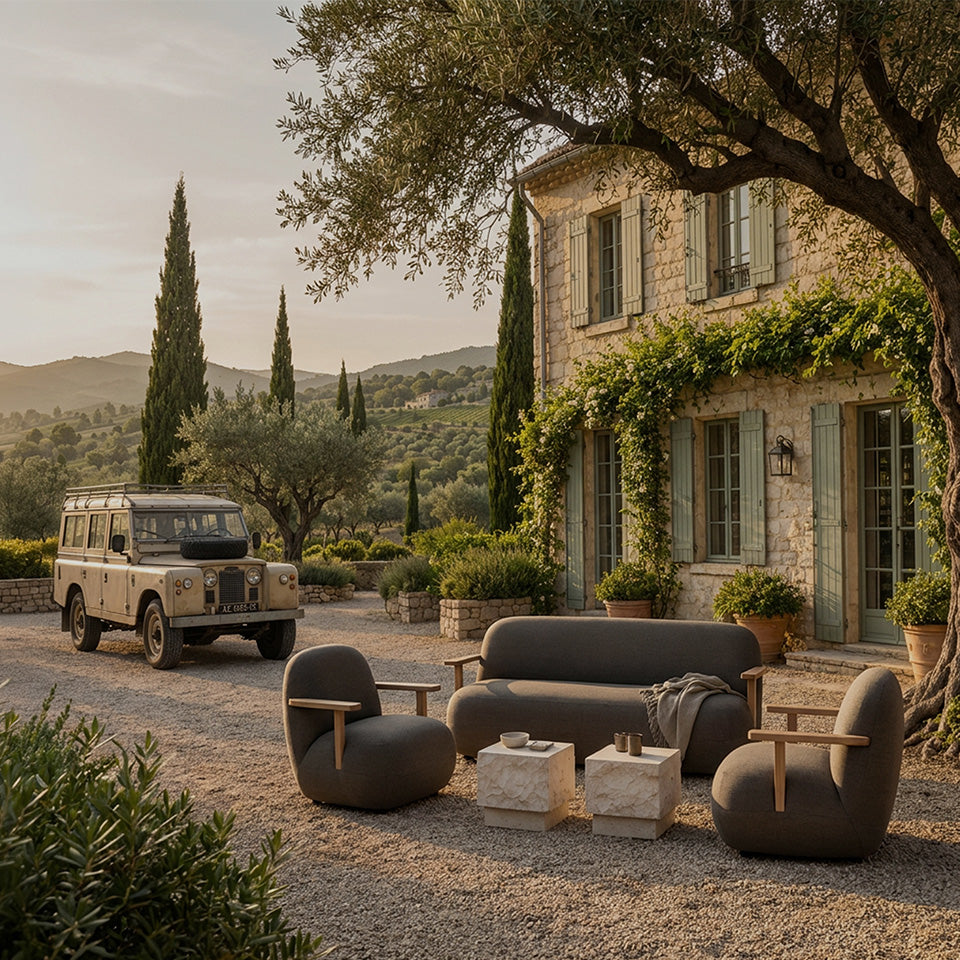 Outdoor Toe furniture set in a rustic stone courtyard beside a vintage Land Rover, with a stone house, trees, and hills in the background.
