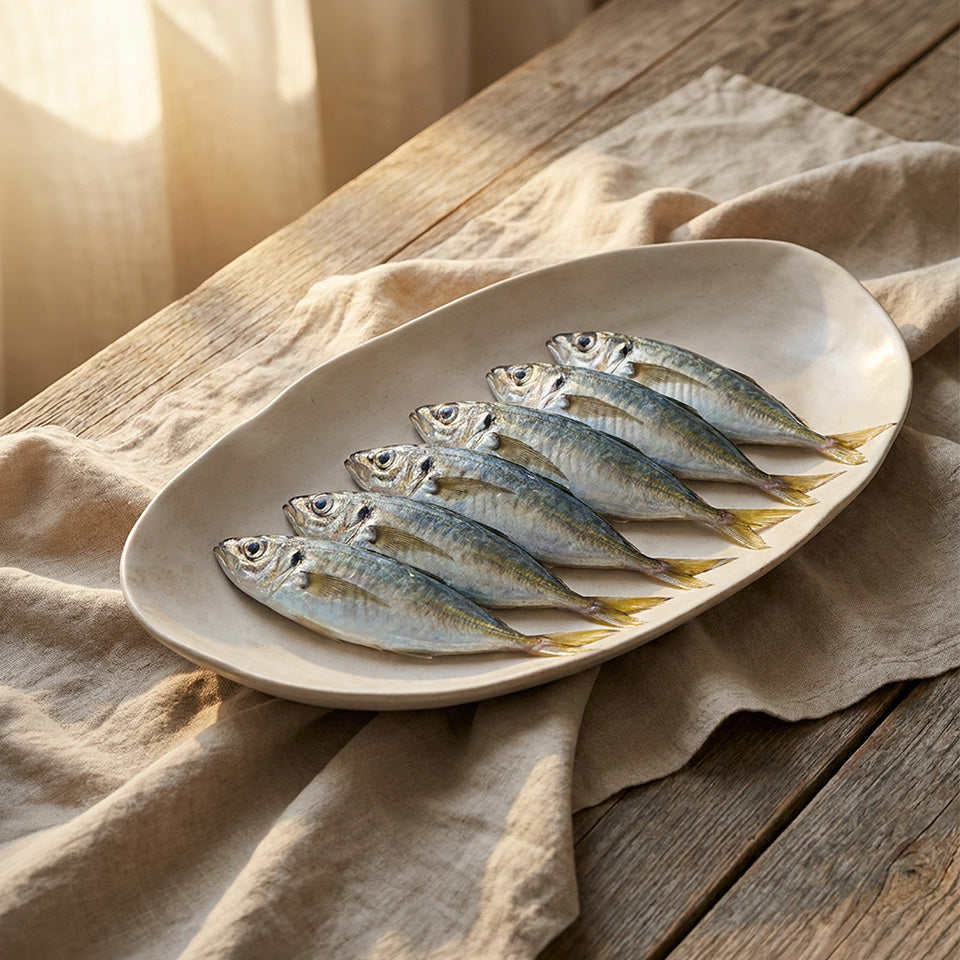 Six small whole fish arranged on an Native oval Tray, set on a draped beige cloth over a rustic wooden table.