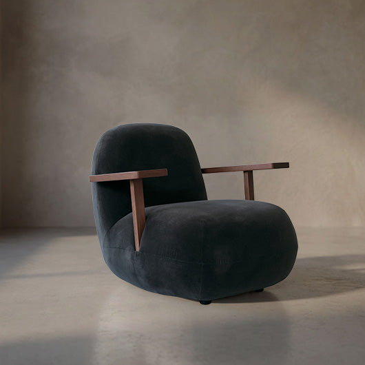 A modern Toe lounge chair with a blue black Peat velvet seat and back, featuring integrated wooden armrests, set against a textured concrete wall and floor.