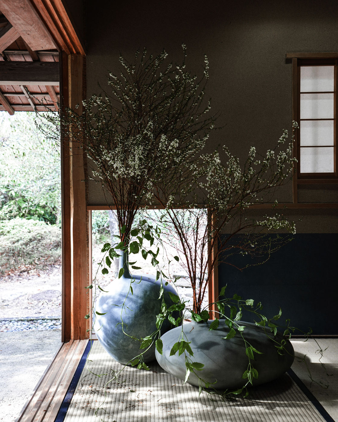 Two large Submarine vases with branches and leaves arranged by Hikaru Seino on a tatami mat floor.